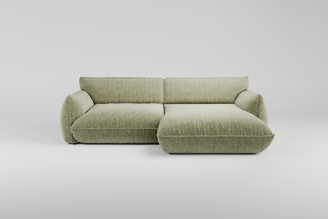 Hellgrünes, modernes L-förmiges Sofa mit breiten Polstern vor einem schlichten weißen Hintergrund.